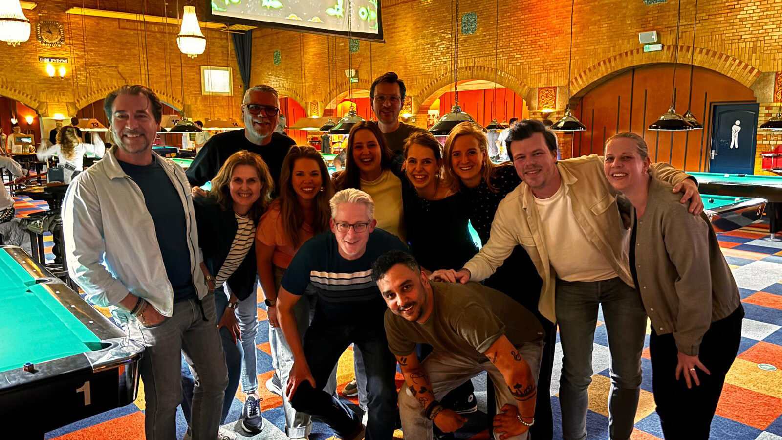 Team Brût poseert lachend in een biljartzaal met meerdere pooltafels