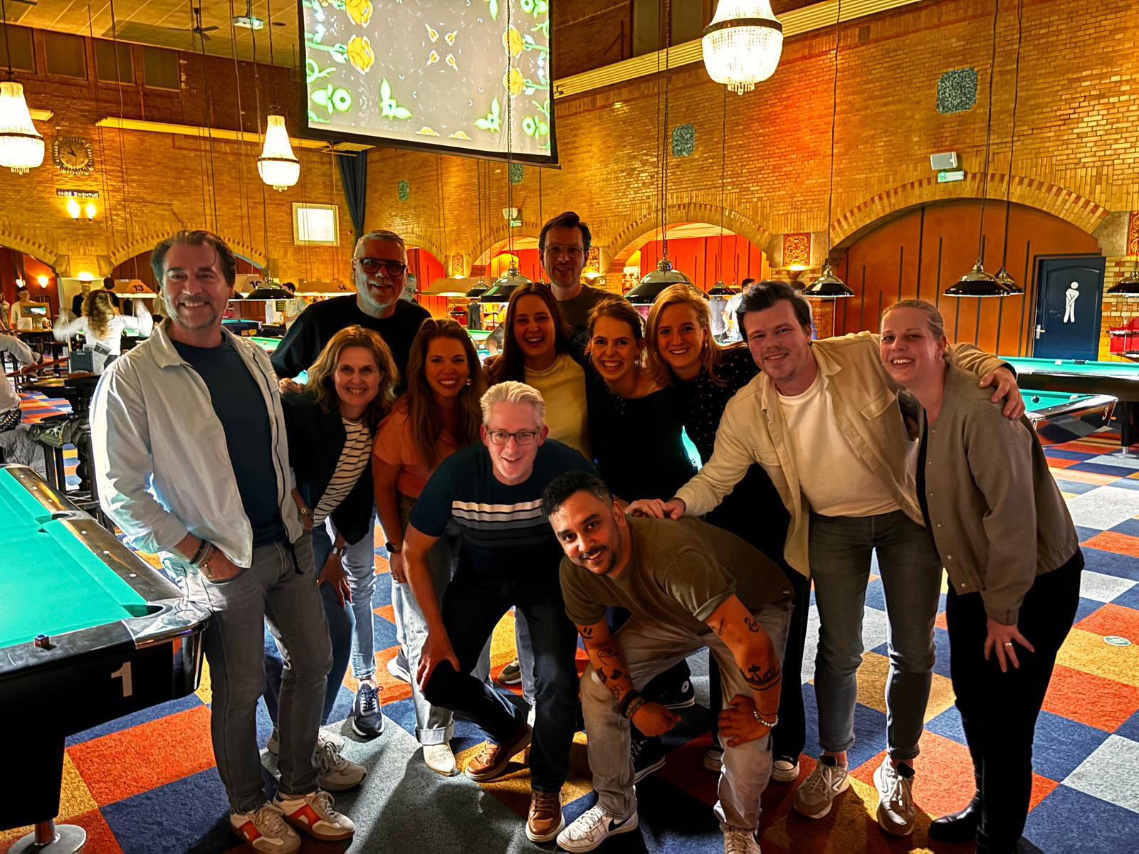 Team Brût poseert lachend in een biljartzaal met meerdere pooltafels