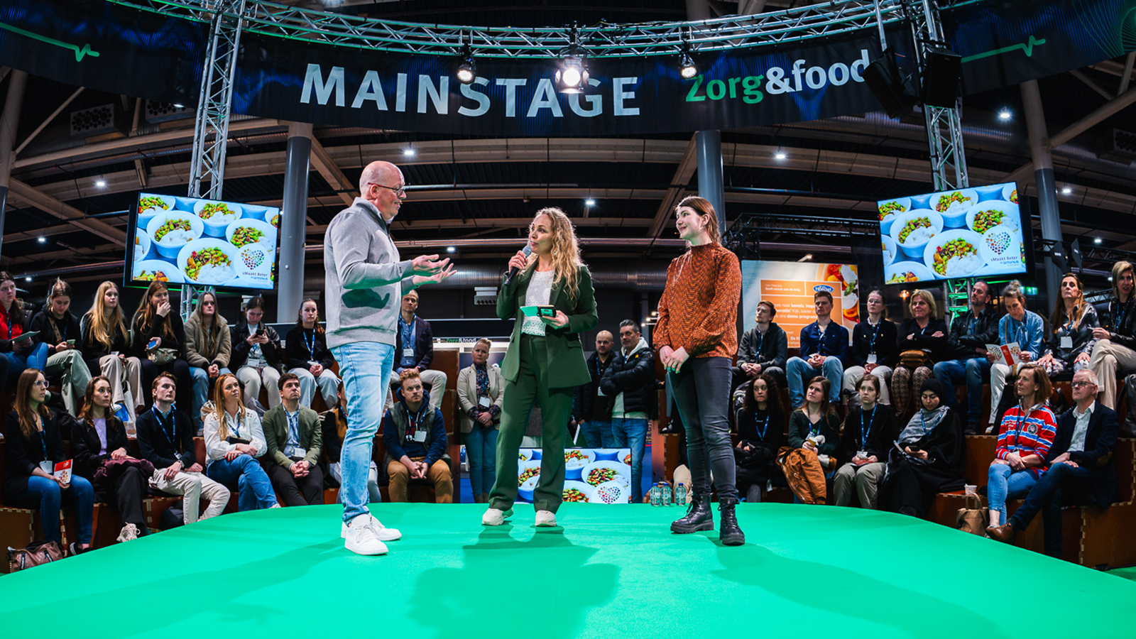 College op de jaarbeurs met drie mensen op het podium