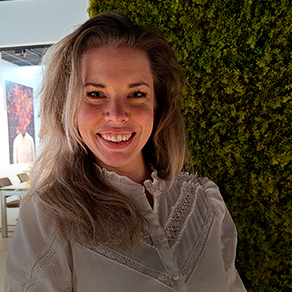 Lachende blonde vrouw in witte blouse, kijkend in de camera voor een groene wand