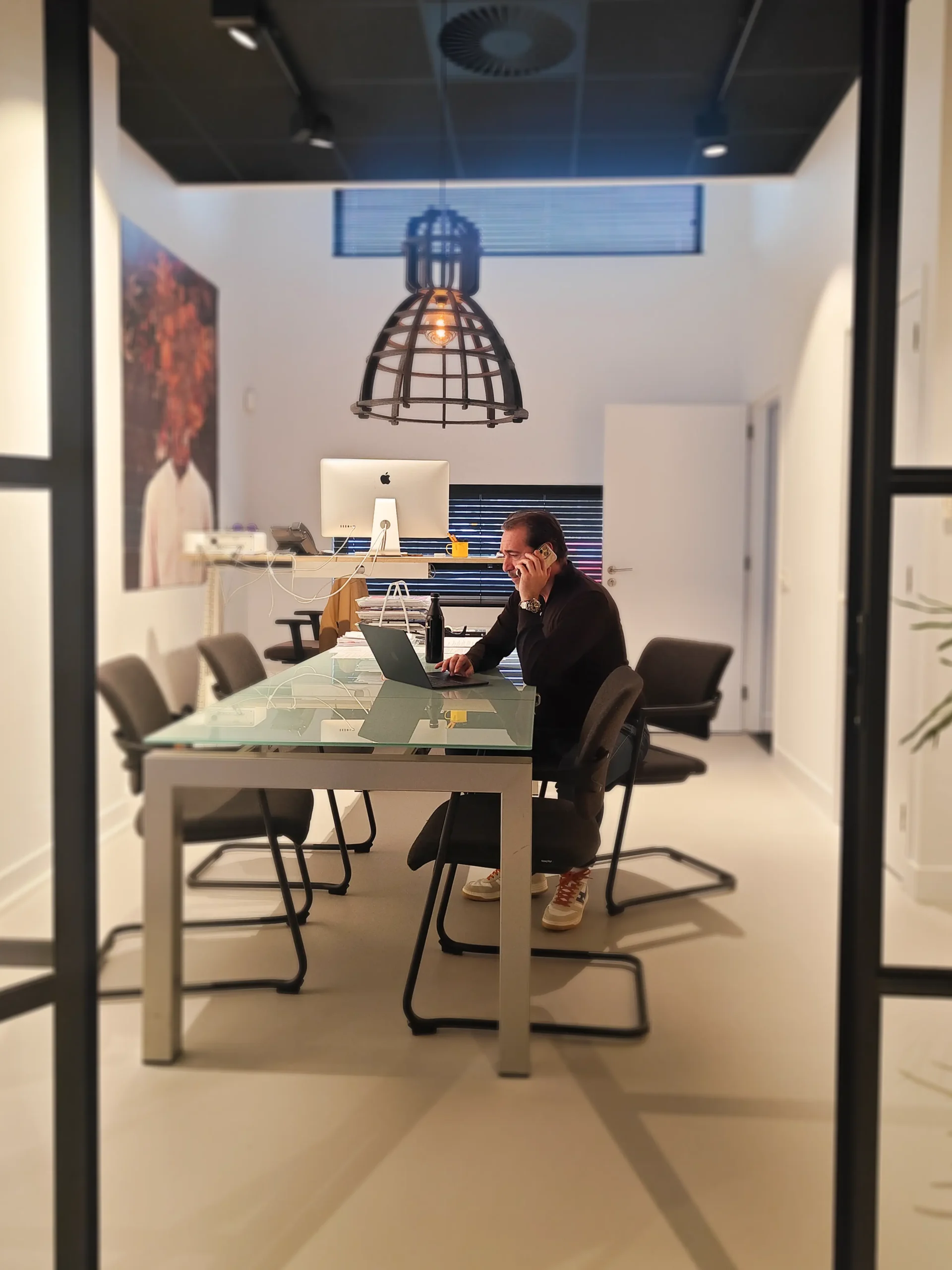 Man zit aan een bureau in een modern kantoor en telefoneert terwijl hij op een laptop werkt