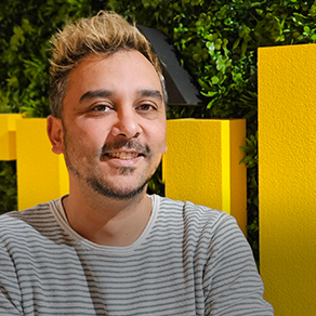 Portret van een glimlachende man met blond haar en gestreept shirt, voor gele panelen en groen blad