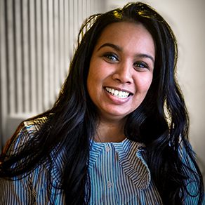 Lachende vrouw in gestreepte blouse, kijkend in de camera voor een verticale lattenwand